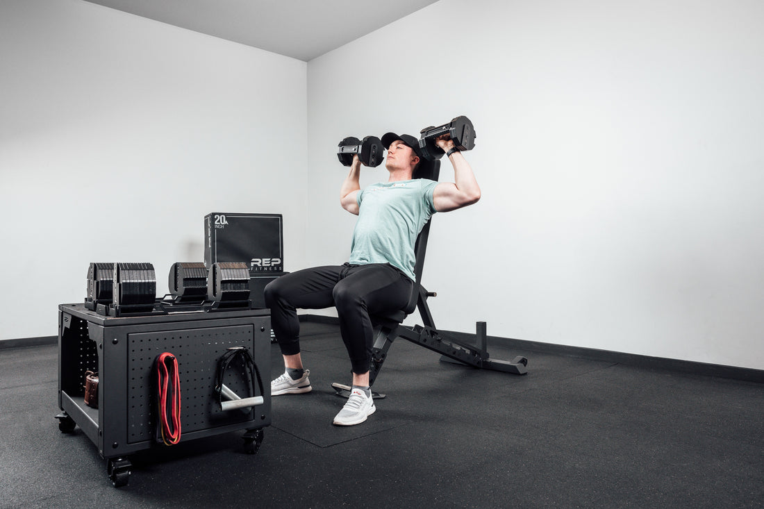 An athlete does a seated shoulder press with adjustable dumbbells.