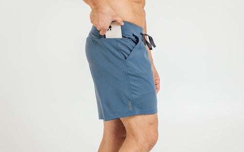 Side view of model sliding his iPhone into the side hip pocket of the heather slate blue REP Versa Shorts.