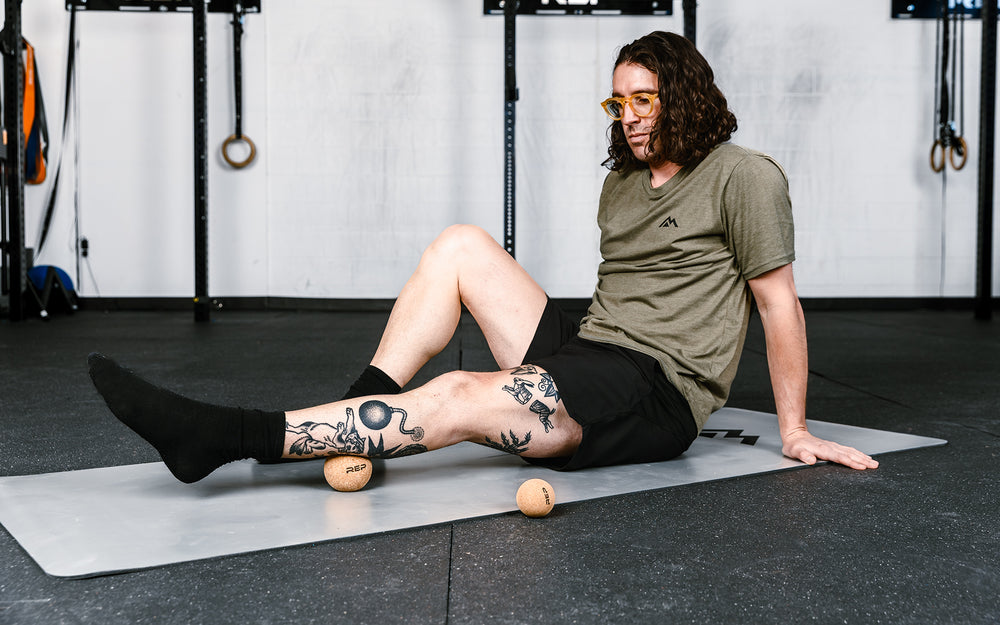 Action-shot: Athlete targeting a pressure point on their leg by rolling the REP Cork Massage Ball against the floor.