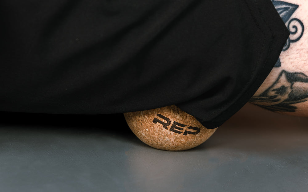 Close-up: Athlete targeting a pressure point on their leg by rolling the REP Cork Massage Ball against the floor.