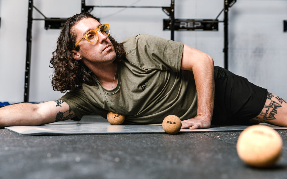 Low-angle shot: Athlete targeting a pressure point on their chest by rolling the REP Cork Massage Ball against the floor.