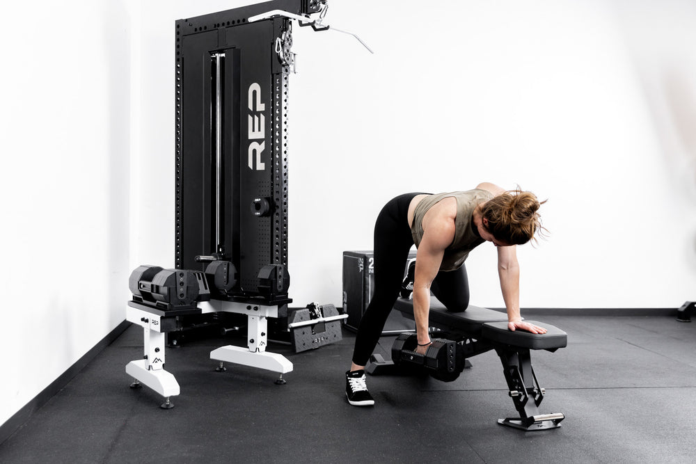 Athlete working out with REP® x PÉPIN™ adjustable dumbbells in front of a white REP® Adjustable Dumbbell Stand