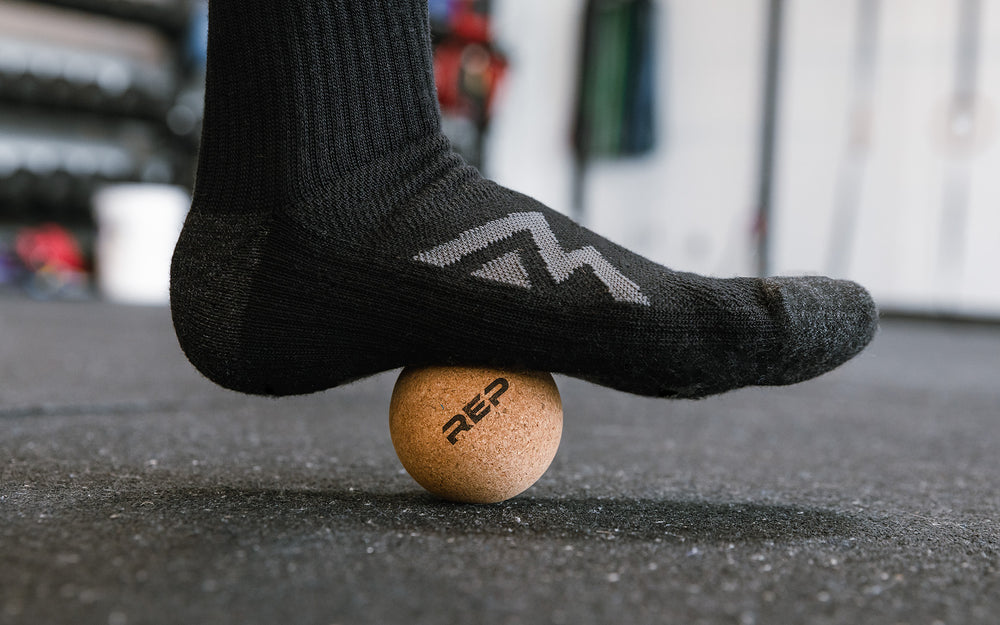 Close-up: Athlete targeting a pressure point on their foot by rolling the REP Cork Massage Ball against the floor.