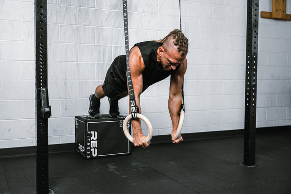 Athlete performing bodyweight pushups on REP Competition Gymnastic Straps and Wood Rings from a REP Soft Plyo box