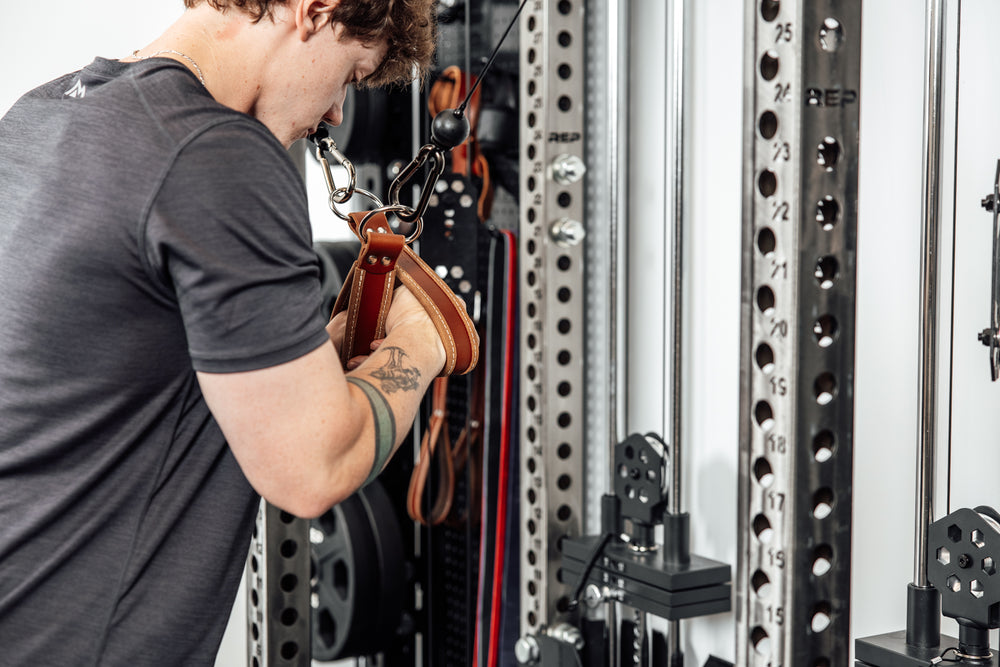 An athlete performing cable crossovers with a pair of REP USA Leather Single Handle Cable Attachments in Brown