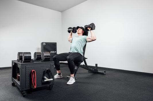 An athlete does a seated shoulder press with adjustable dumbbells.