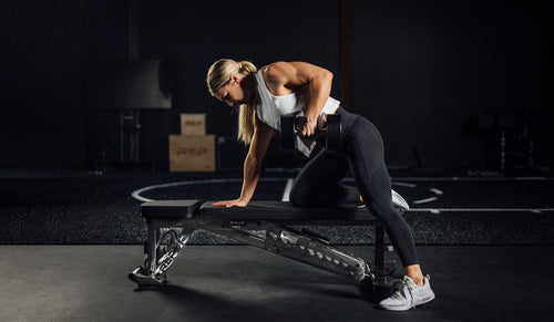 A woman tackles a row while stabilizing herself on an adjustable bench.
