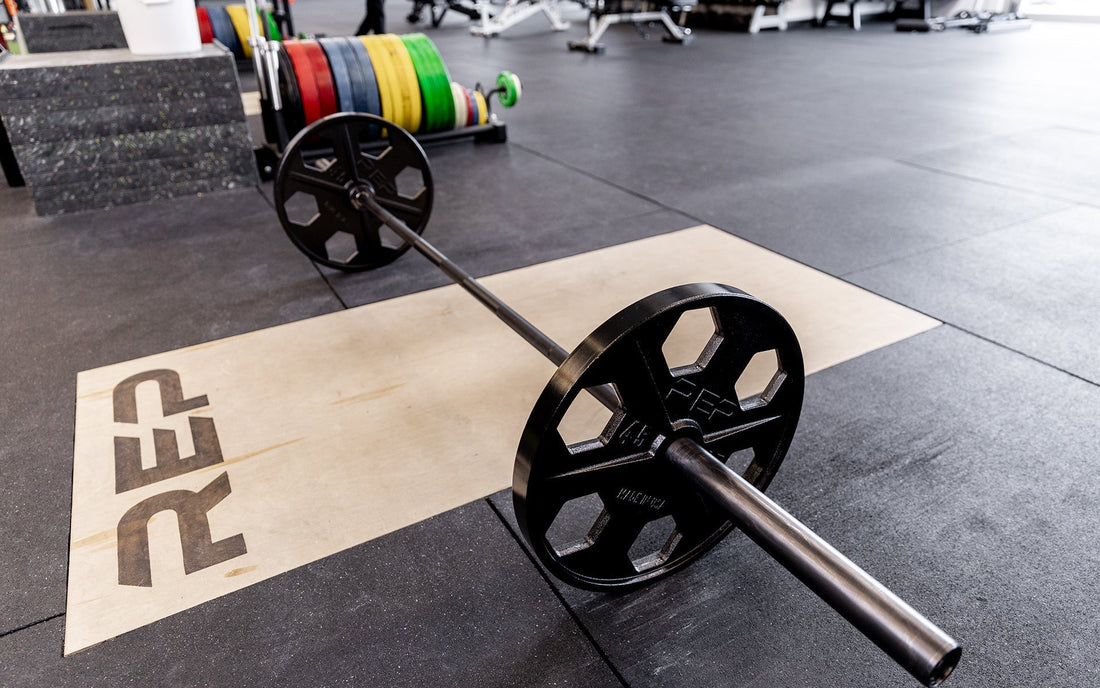 Barbell loaded with REP USA-Made Equalizer™ Iron Plates on a platform with bumper plates in the background