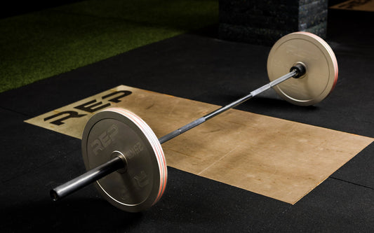A loaded barbell sits on a deadlift platform in a gym.