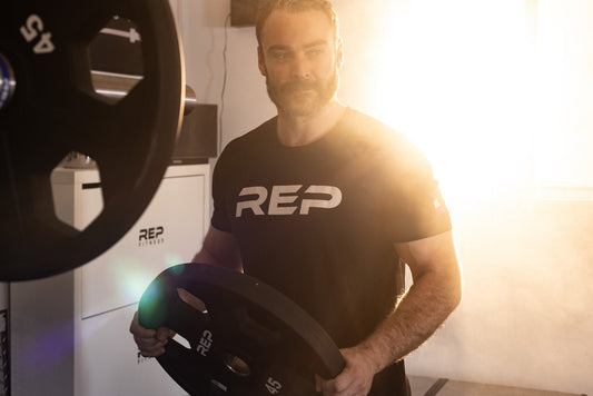 An athlete in a REP® t-shirt loads 45-pound weight plates onto a bar.