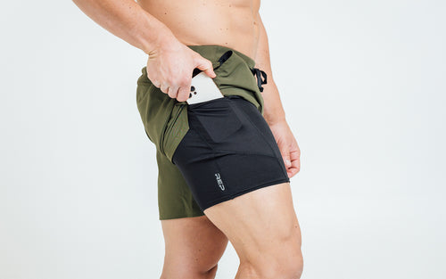 Side view of model sliding his iPhone into the side pocket of the REP Virtus Light Compression Shorts.