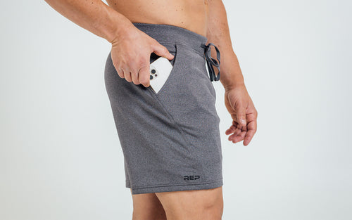 Side view of model sliding his iPhone into the side pocket of his cool gray REP Attis shorts.