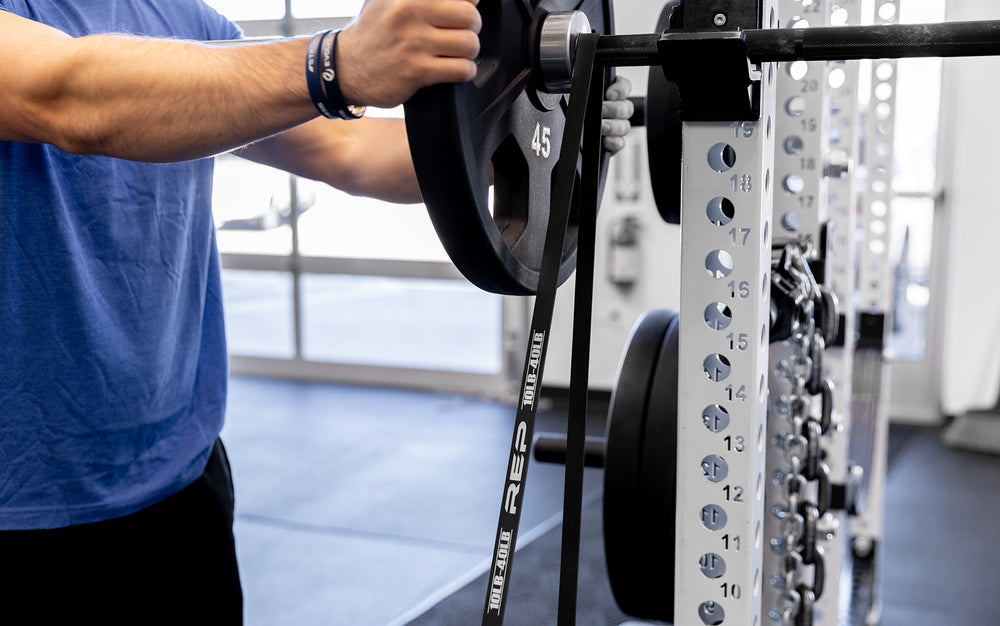 Close-up view of a black Latex-Free Pull-Up Band being set up on a racked barbell for added resistance while squatting.