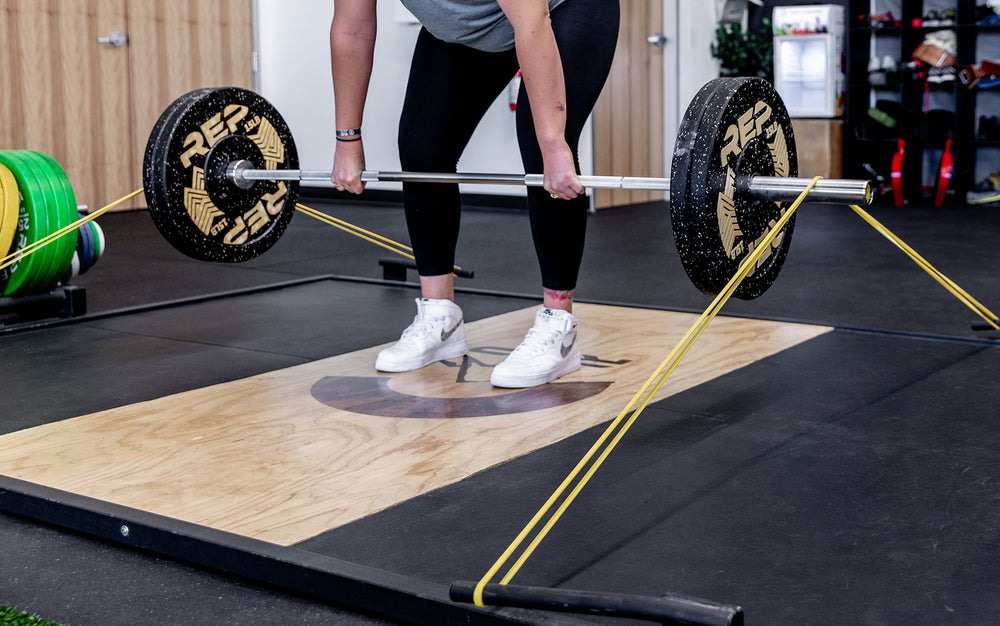 Athelete Athlete using a pair of yellow Latex-Free Pull-Up Bands for added resistance while deadlifting.