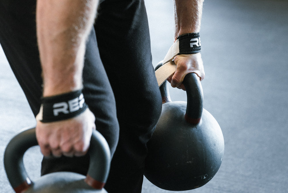 Lifter deadlifting a pair of kettlebells while wearing REP Lifting Straps.