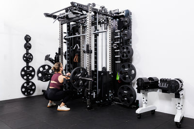 Person performing front squats off the front of the Summit™ All-In-One Ares™ 2.0 Wall-Mounted configuration in a gym setting.