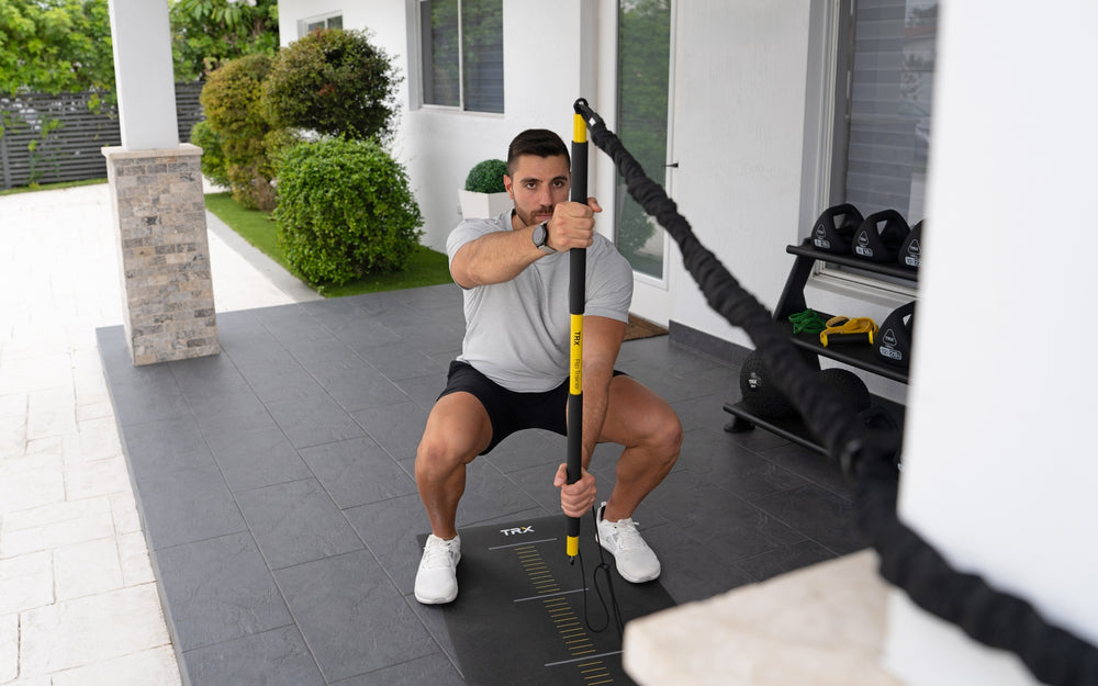 Front shot: Athlete squatting with the TRX® Rip Trainer™ at perpendicular to the ground in front of them
