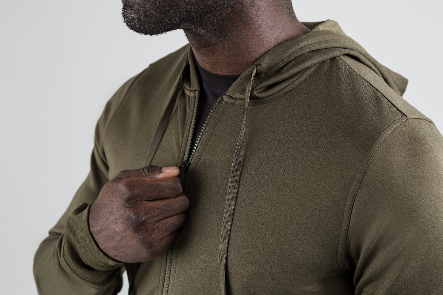 Men's Hoodies and Jackets - Close up of man zipping up the heather olive Attis Jacket with a background.