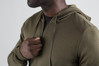 Men's Hoodies and Jackets - Close up of man zipping up the heather olive Attis Jacket with a background.