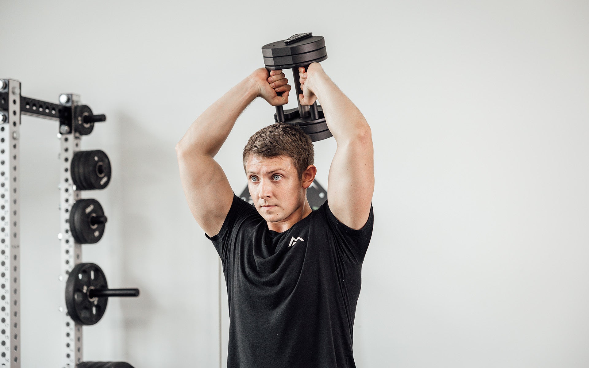 Male lifter standing and performing french presses with a single REP Fitness QuickDraw Adjustable Dumbbell.