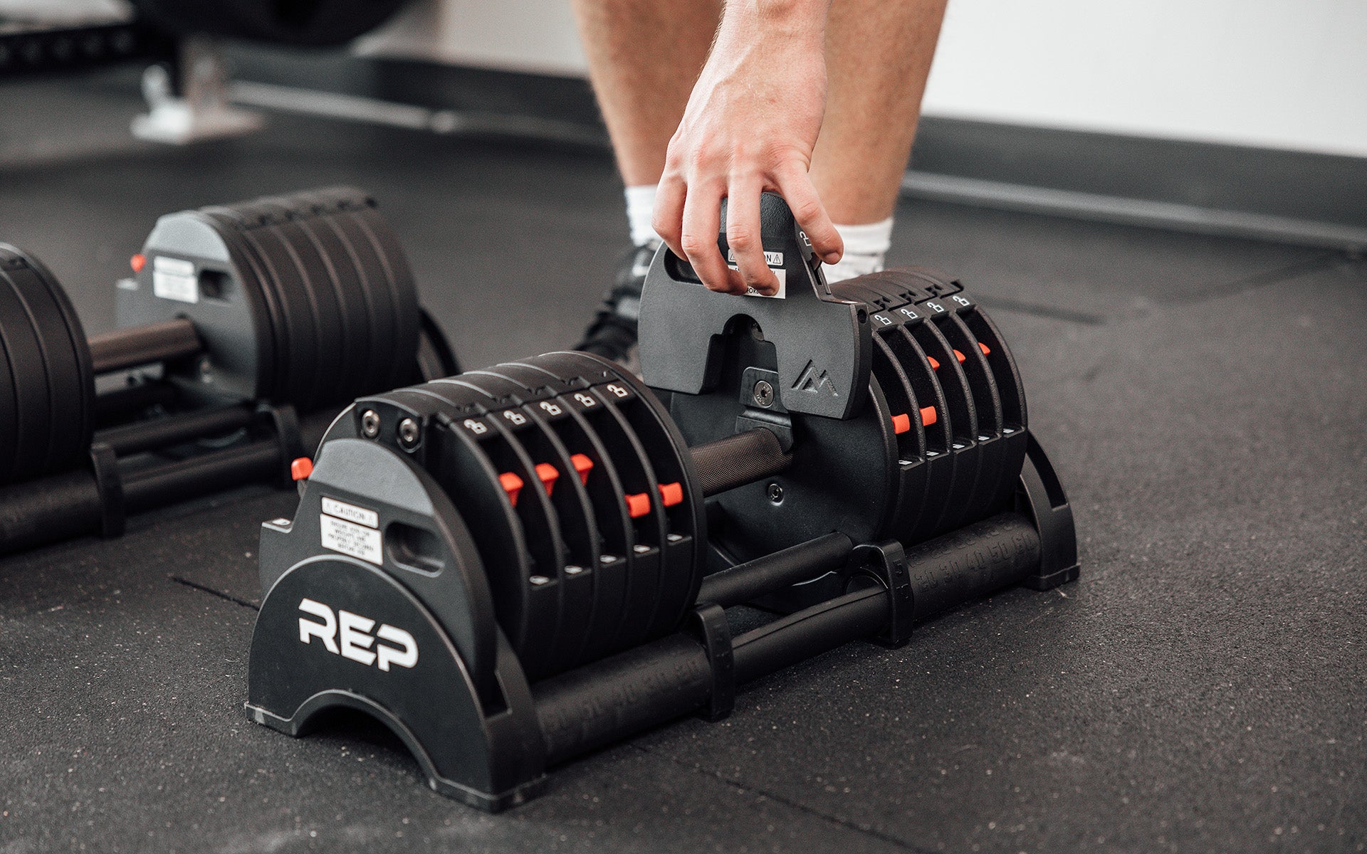 Close-up view of a lifter adding on a 2.5lb microplate to a 60lb REP Fitness QuickDraw Adjustable Dumbbell.