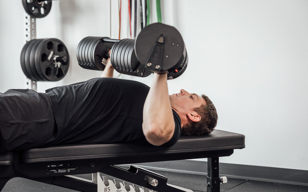 Male lifter performing bench presses with a pair of REP Fitness QuickDraw Adjustable Dumbbells.