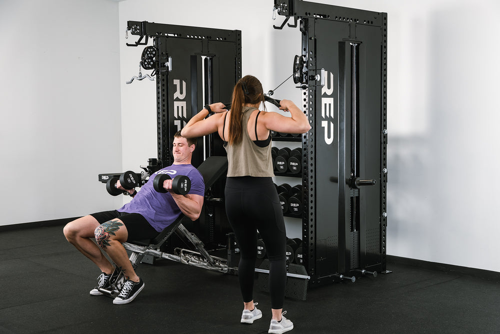 2 people training at the same time on the Dual Adonis™ with Storage setup. One using one Adonis™ Cable Tower while the other using a bench in the middle.