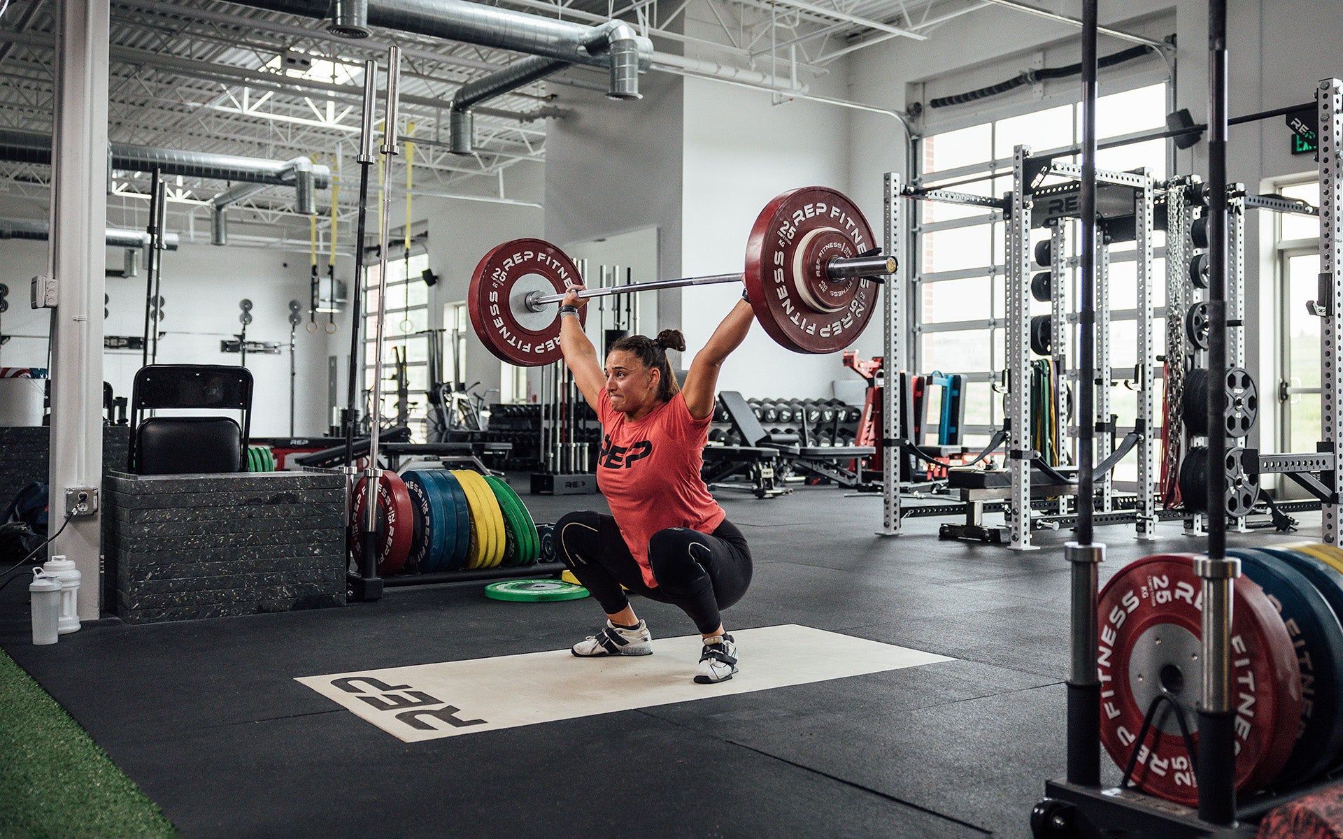 Female lifter in the bottom of a snatch on an Olympic lifting platform using REP's 15kg Alpine Weightlifting Bar.