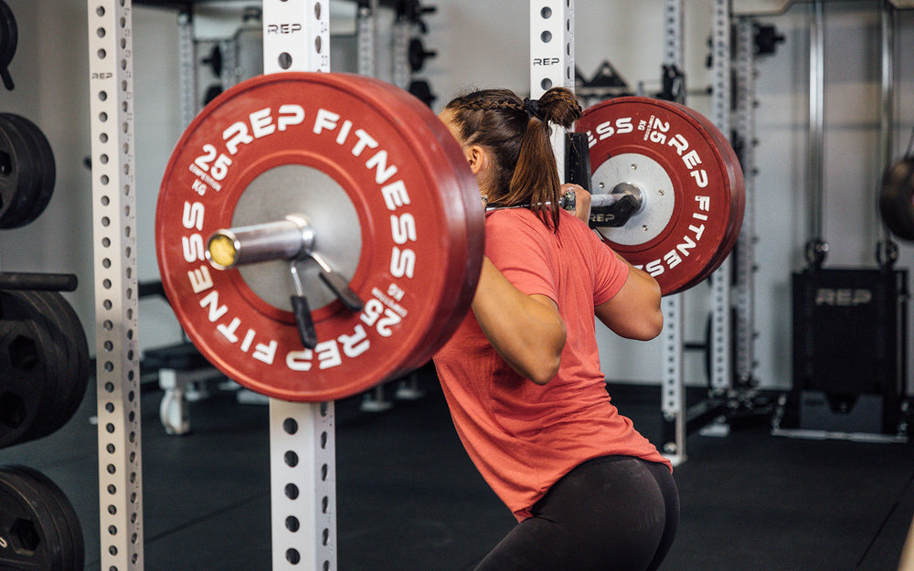 Female lifter back squatting with a REP 15kg Alpine Weightlifting Bar in a REP power rack.