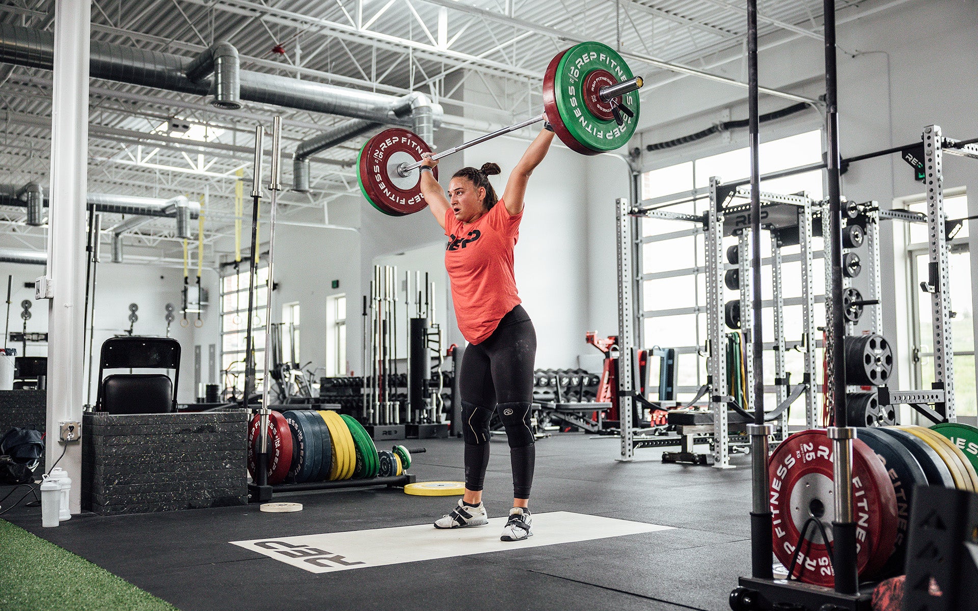 Female lifter performing a snatch on an Olympic lifting platform using REP's 15kg Alpine Weightlifting Bar.