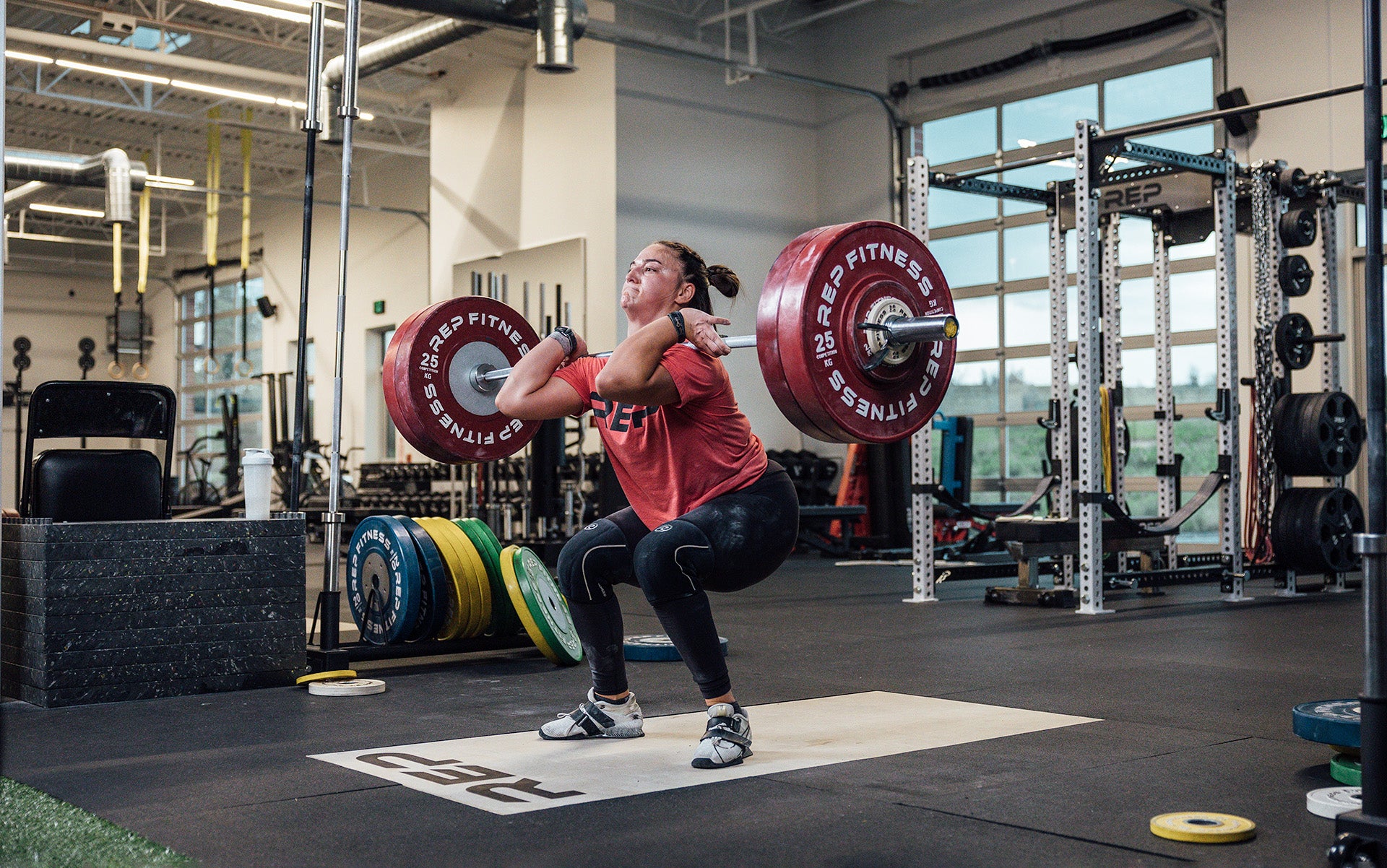 Female lifter performing a clean and jerk on an Olympic lifting platform using REP's 15kg Alpine Weightlifting Bar.