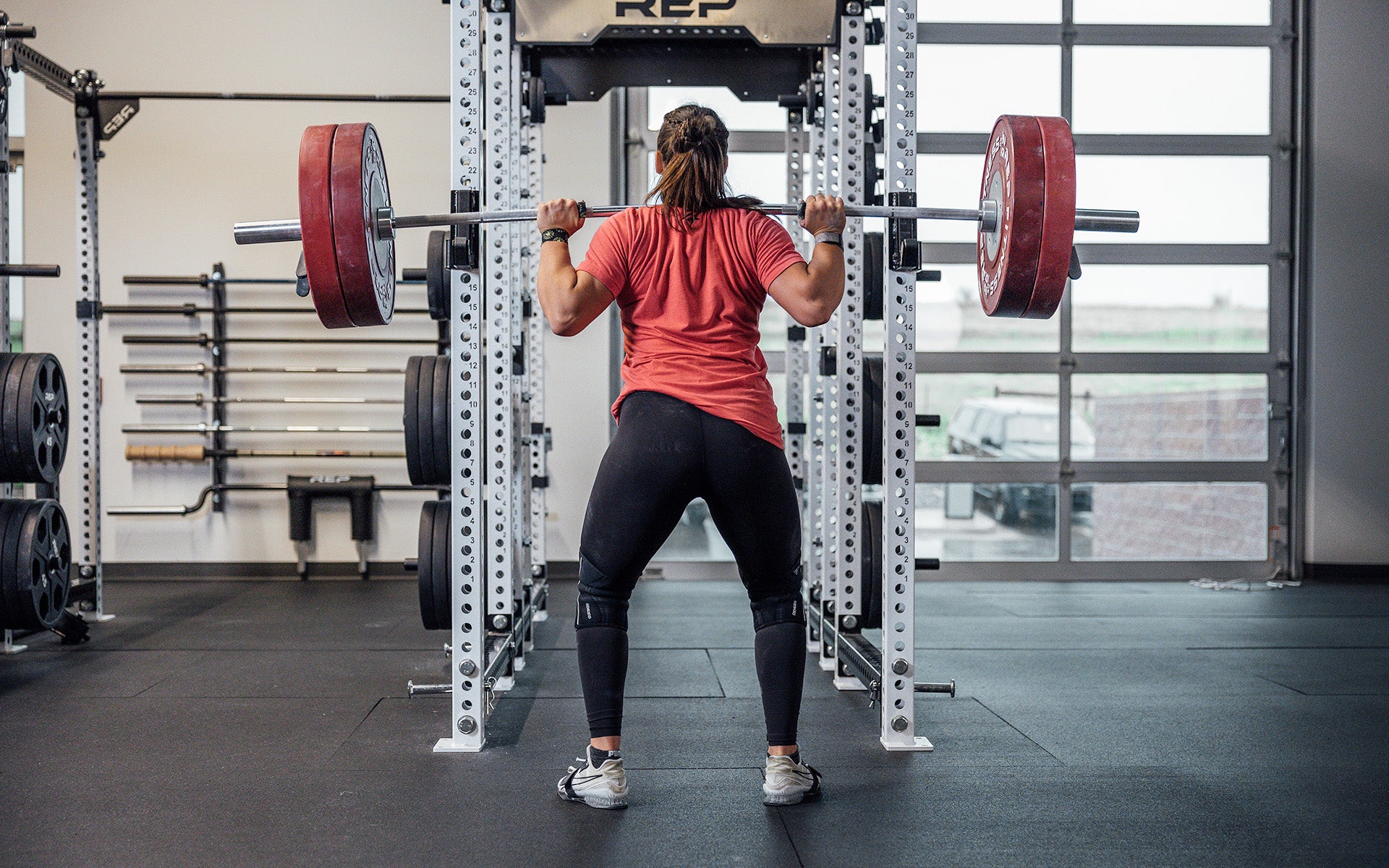 Female lifter back squatting with a REP 15kg Alpine Weightlifting Bar in a REP power rack.