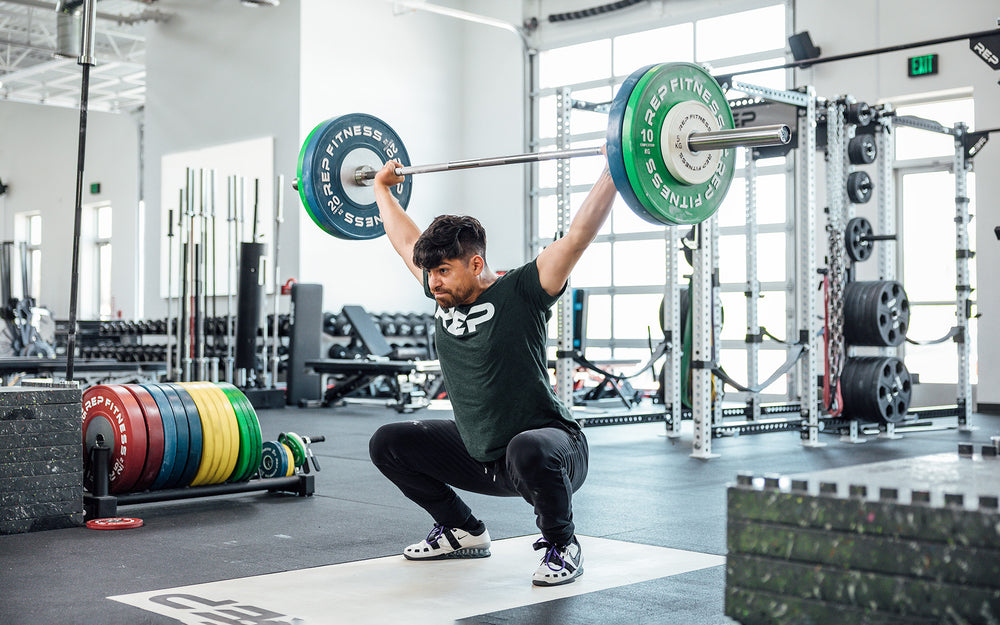 Male lifter in the bottom of a snatch on an Olympic lifting platform using a REP 20kg Alpine Weightlifting Bar.