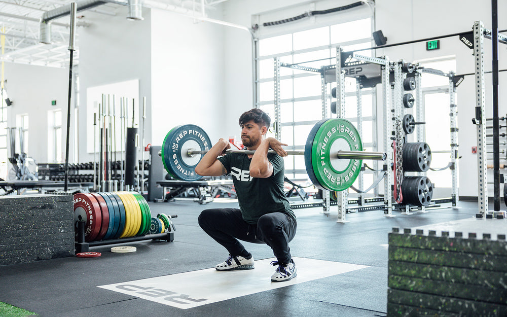 Male lifter in the bottom of a clean and jerk on an Olympic lifting platform using a REP 20kg Alpine Weightlifting Bar.