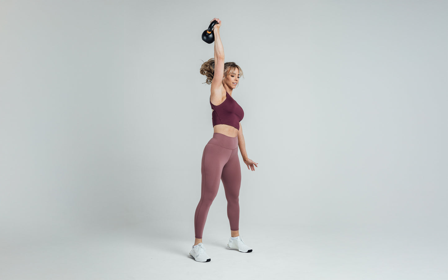 Athlete holding a kettlebell over their head while wearing the REP Rhea Tank in Wine