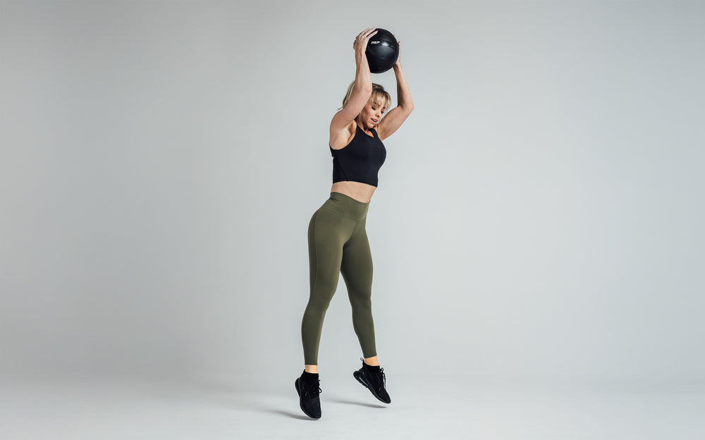 Side shot of an athlete mid-movement getting ready to throw a slam ball while wearing the REP Rhea Tank in Black.