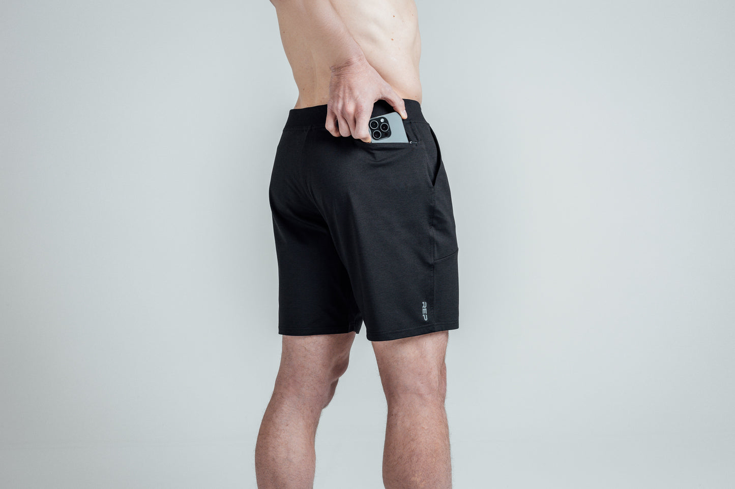 Close-up shot of an athlete putting his phone in the zipper pocket of REP’s Men’s Apollo Shorts in 
Heather Black/Cool Gray