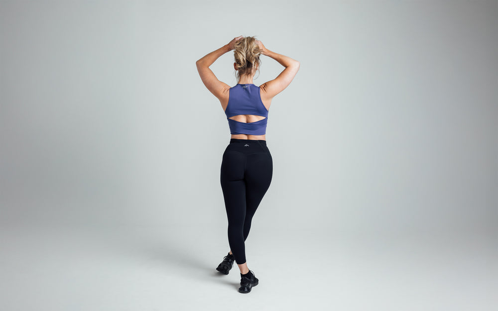 Back shot of an athlete stretching her arms above her head while wearing the REP Rhea Tank in Dusk.