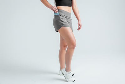Front angled shot: Athlete putting their phone into the pocket of the Cool Gray Women’s Artemis Shorts