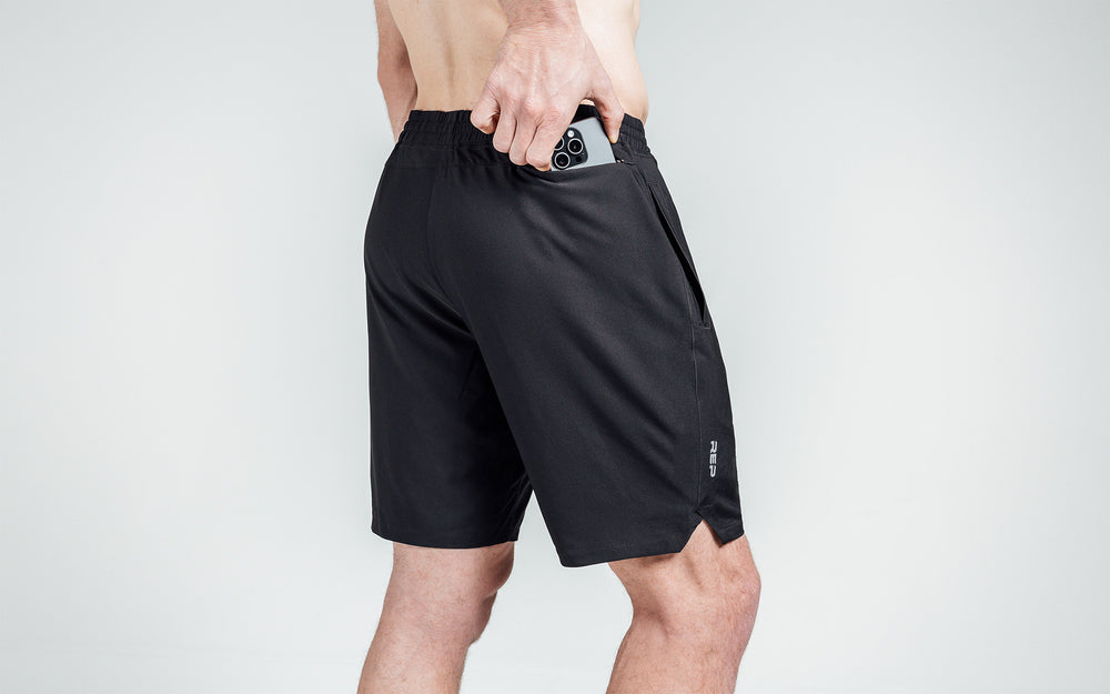 Athlete putting a phone in the zipper pocket of black Motus Shorts