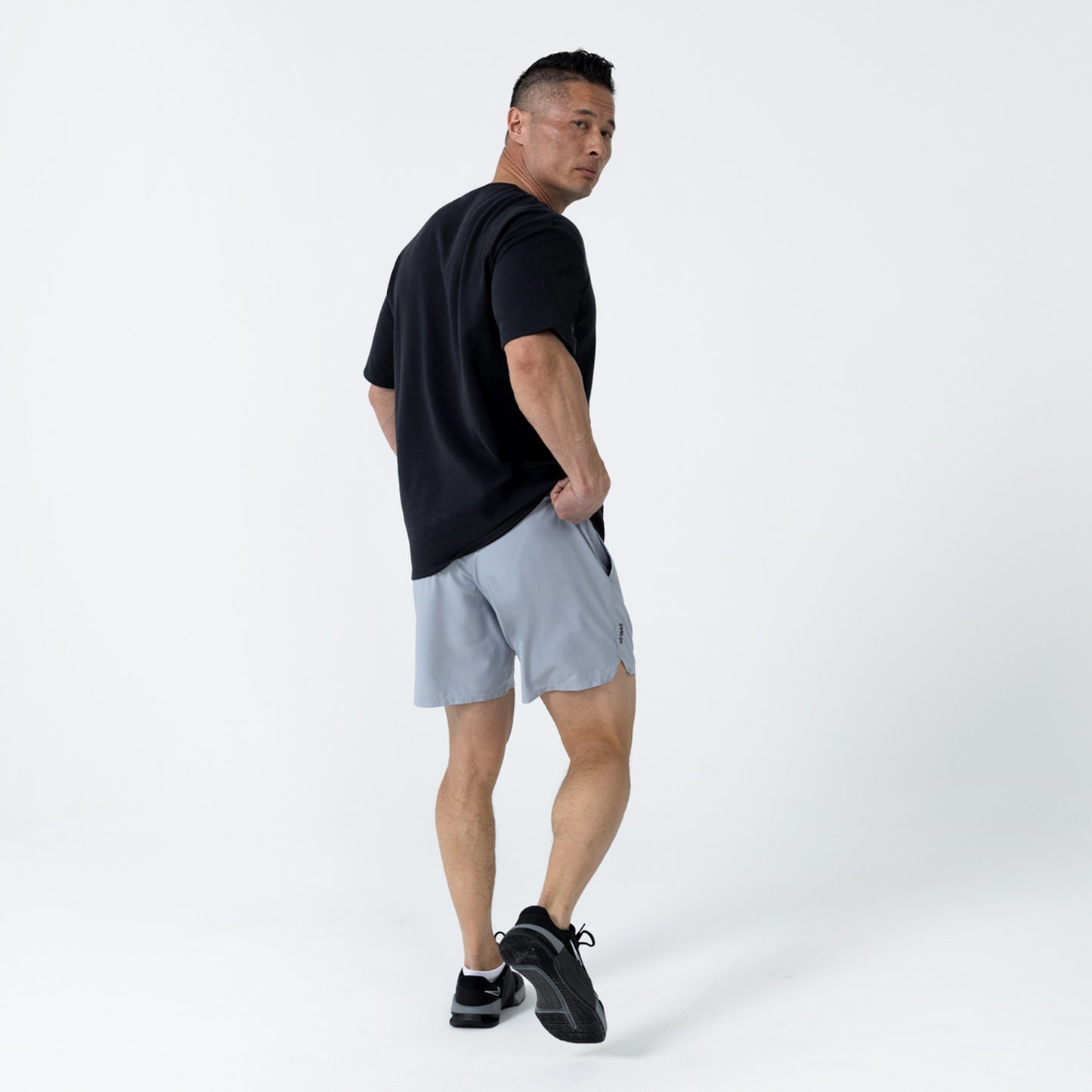 Men's Magnis Heavyweight T-Shirt in Black on person with grey shorts on a white background. back profile.
