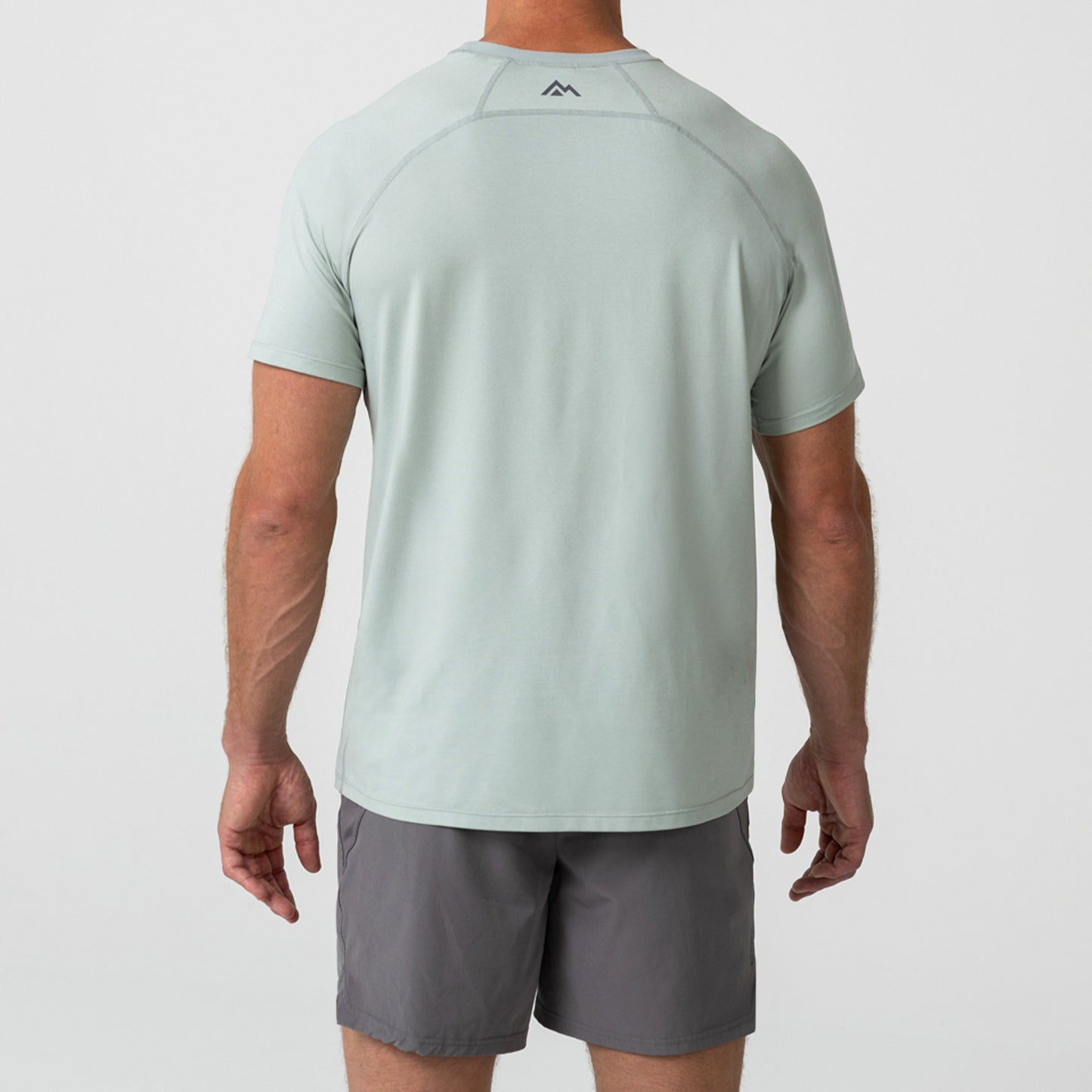 Person wearing an aqua gray Men's Aerix athletic shirt with a mountain logo on the back, standing against a light background.