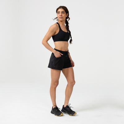 Woman wearing black athletic Women's Vellus shorts and black sports bra on a white background. front view.