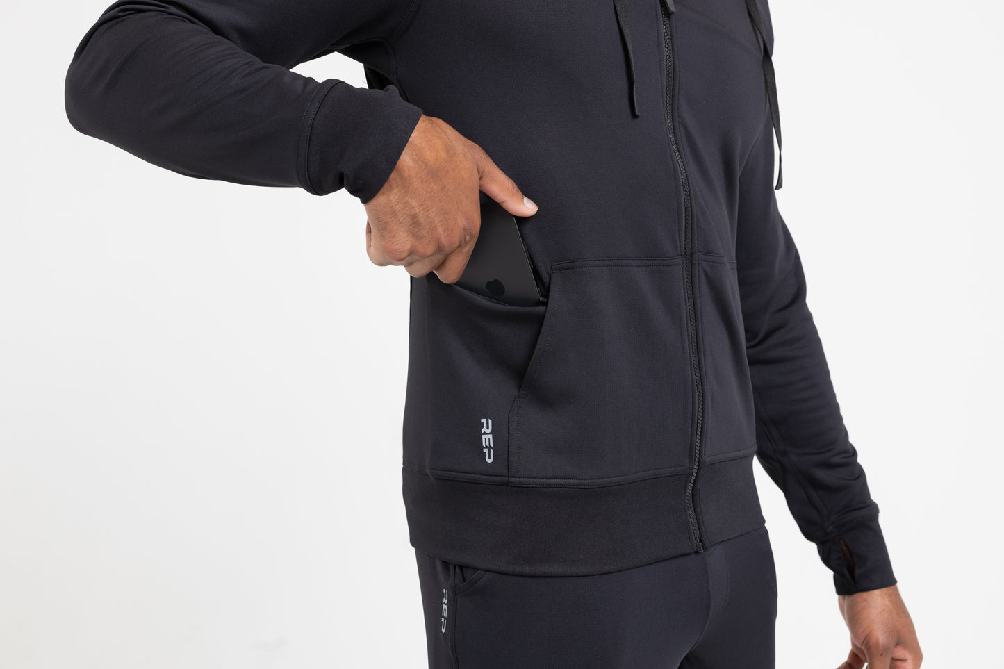 Person sliding their phone into the hidden side zipper pocket on the heather black Attis Jacket
