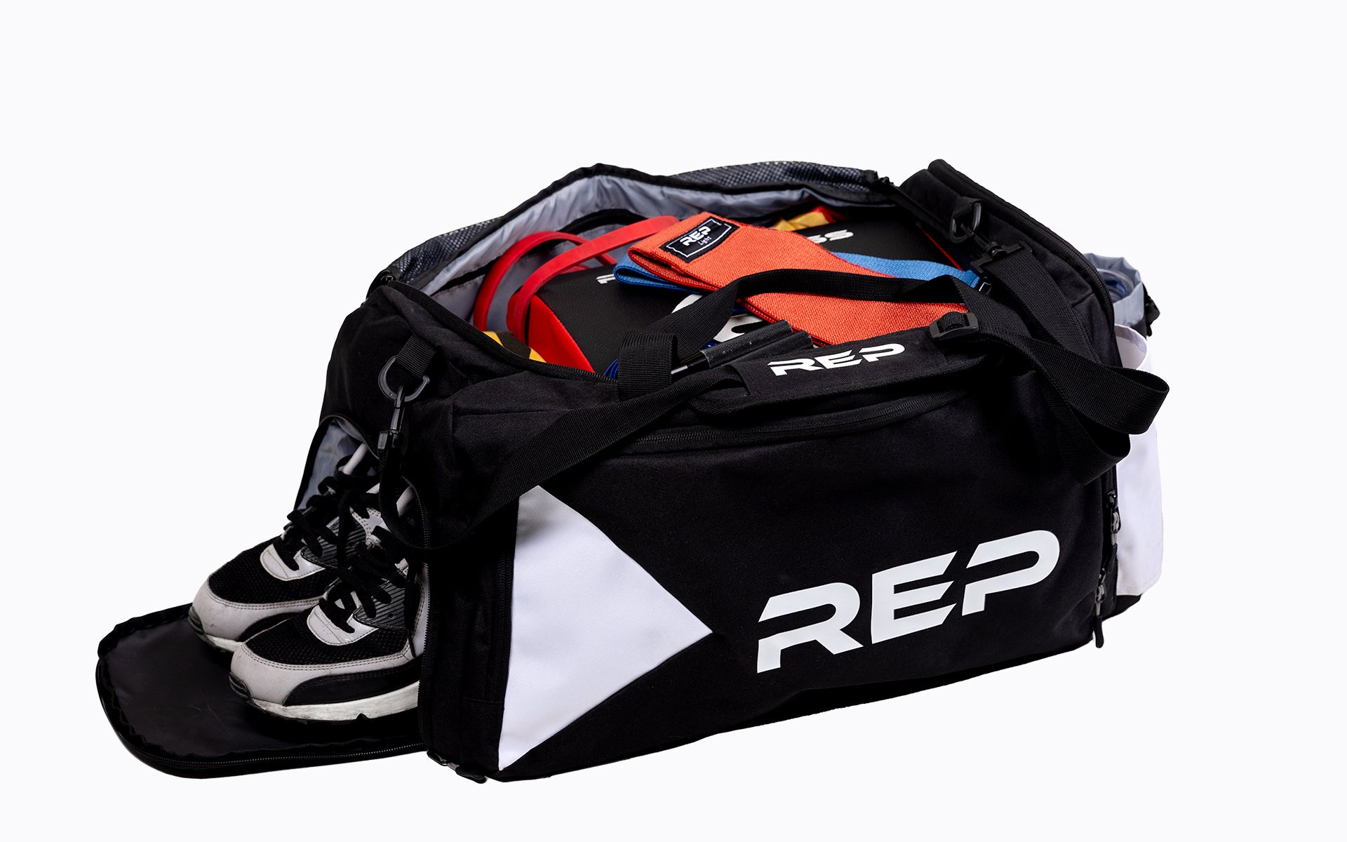 Angled View of REP gym bag full of gym accessories such as shoes, hip circle bands, pull-up bands, ab mat, and more