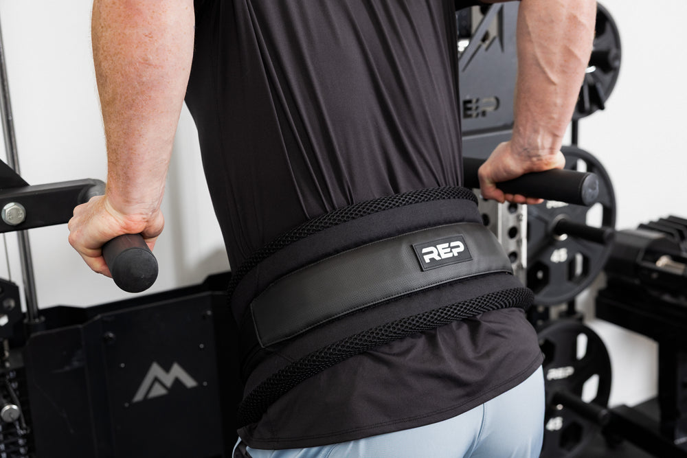 Person using gym equipment and belt squat belt with REP logo for weighted dips.