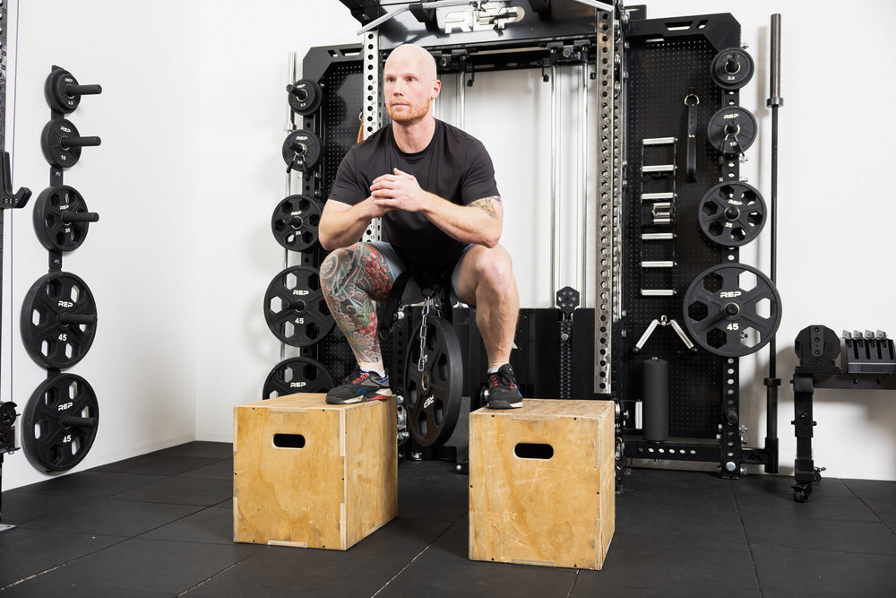 Person using the belt squat belt to do weighted squats. Using two plyo boxes to stand on top of while the weight dangles from the belt in between.