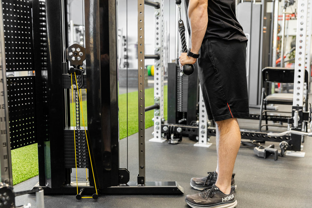 Lifter performing tricep rope pushdowns on the REP Arcadia Functional Trainer while using yellow short resistance bands for added resistance.