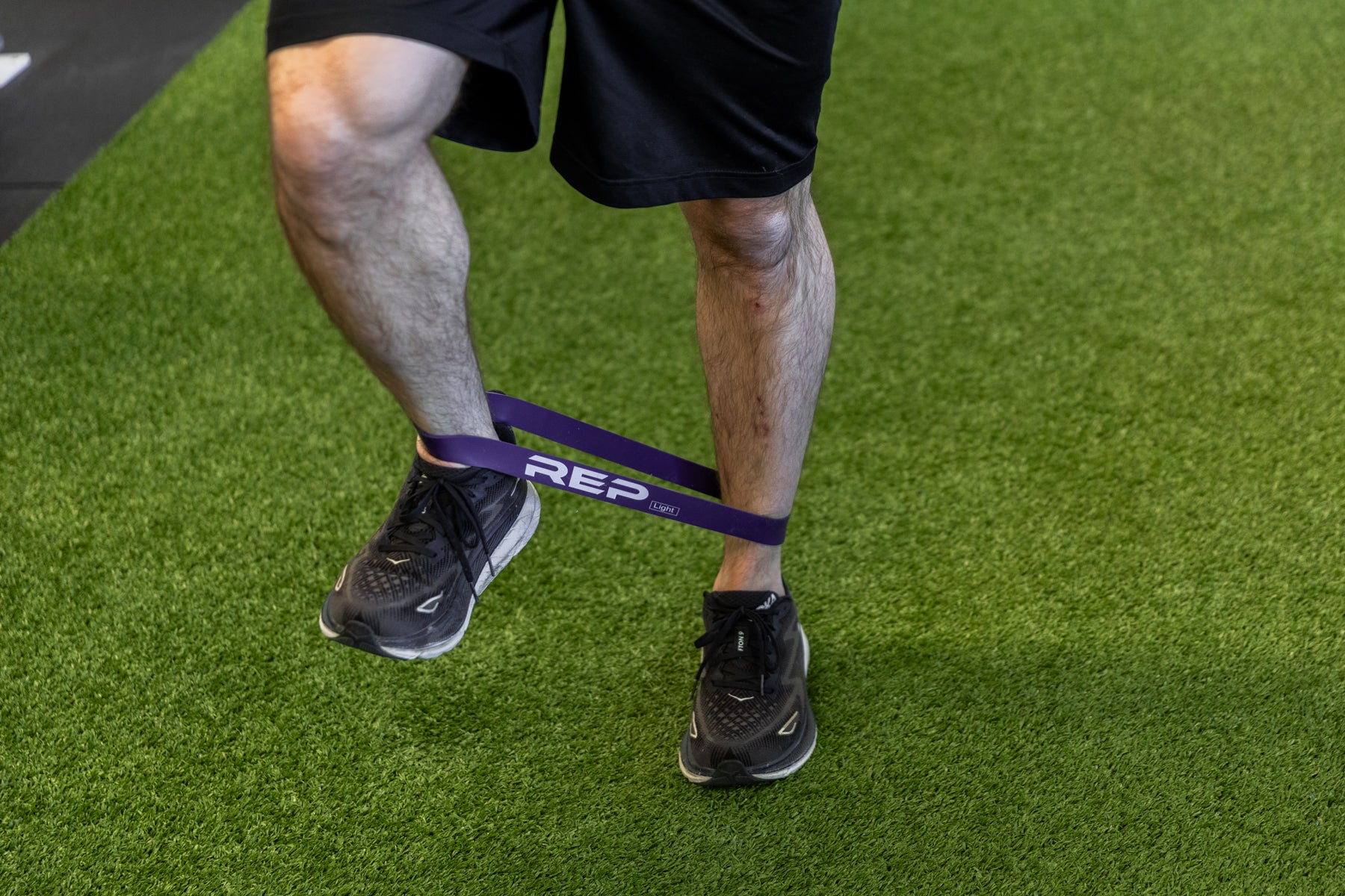 Athlete using a purple short resistance band around his lower leg for agility exercises.
