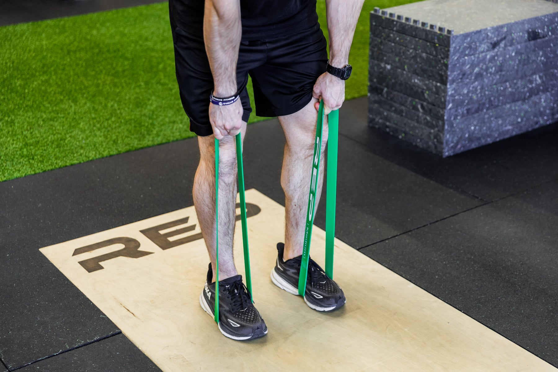 Lifter using green short resistance bands around his feet to perform banded deadlifts.